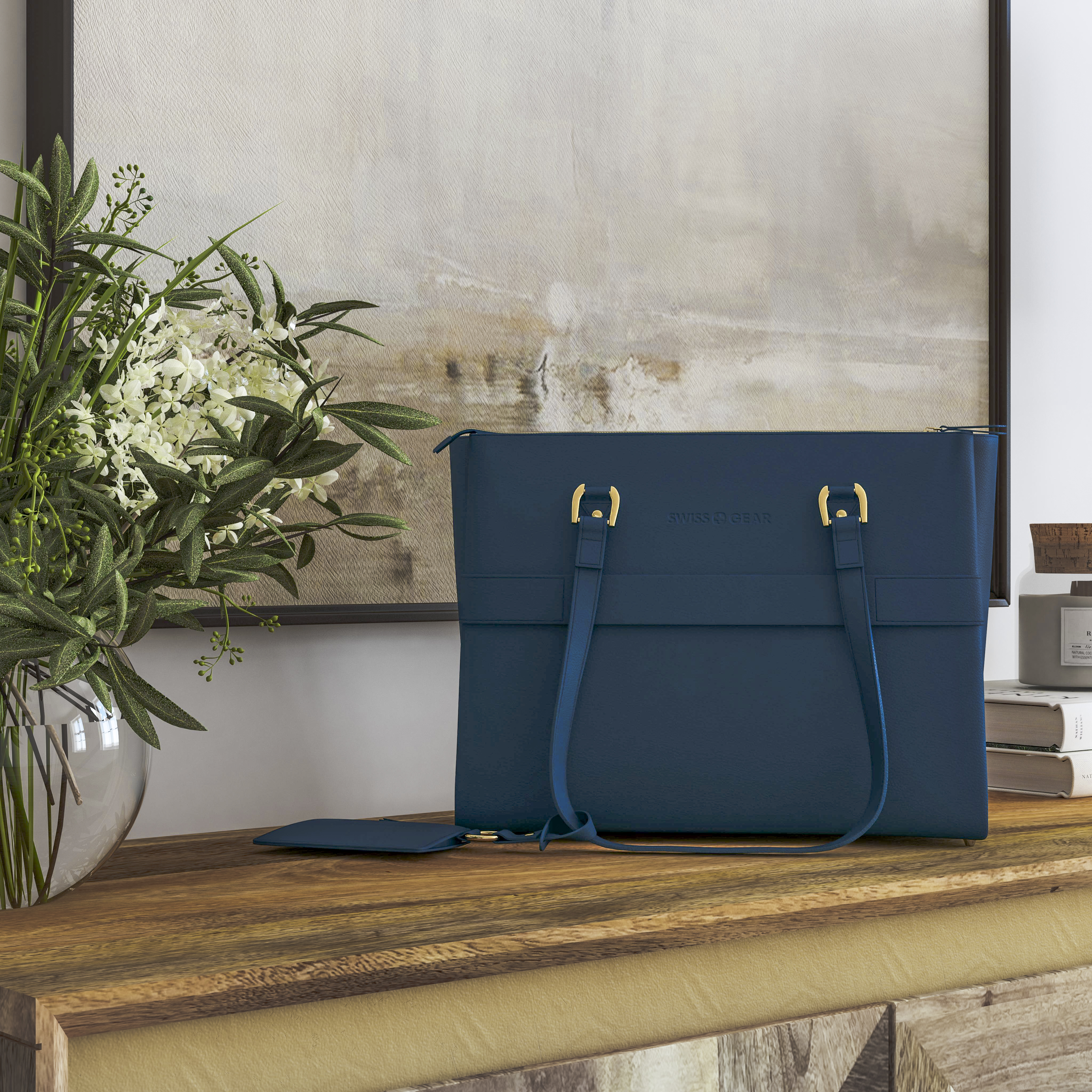 Blue handbag styled on a wood surface with flowers, books, and abstract art